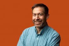 photo of smiling researcher Scott Baker from EMSL in front of an orange background