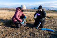 two people kneel in the soil to collect core samples