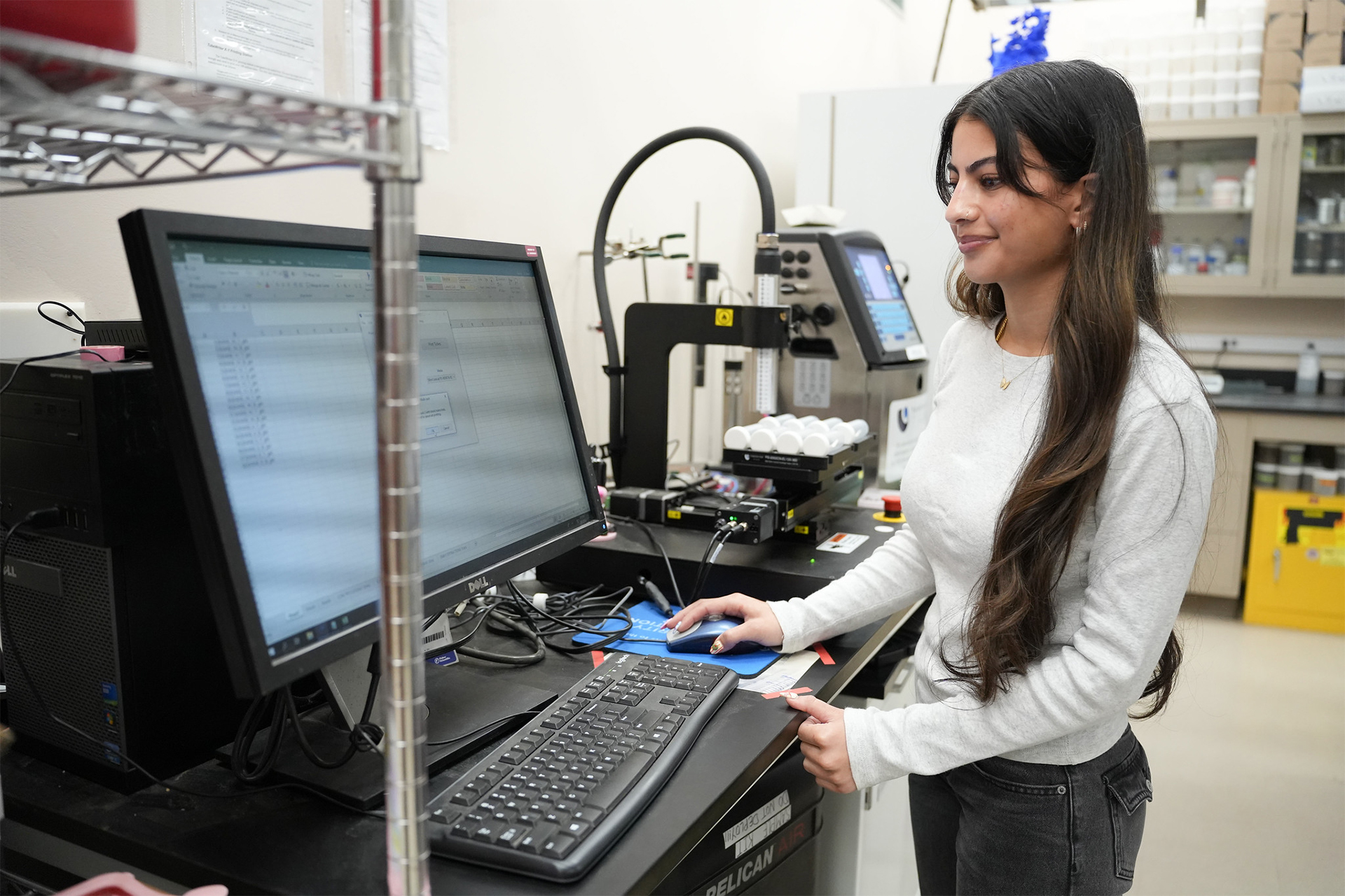 Photo of researcher Ruqaya Talib standing at a laboratory station, looking at a computer monitor.