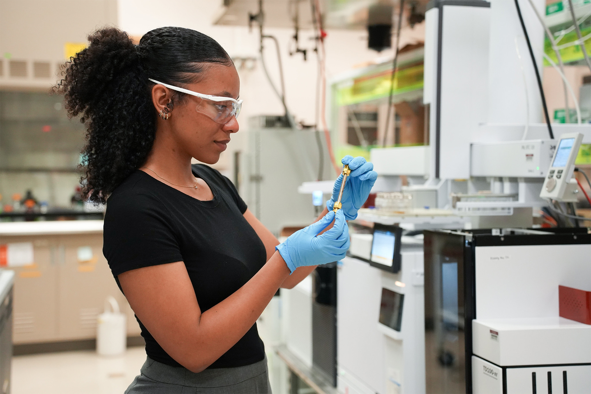 Photo of researcher Cheyanne Williams standing in a laboratory setting, looking at a test tube.
