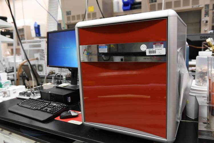 photo of the red C, H, N, S Analyzer sitting on a desk with a computer and keyboard to the left