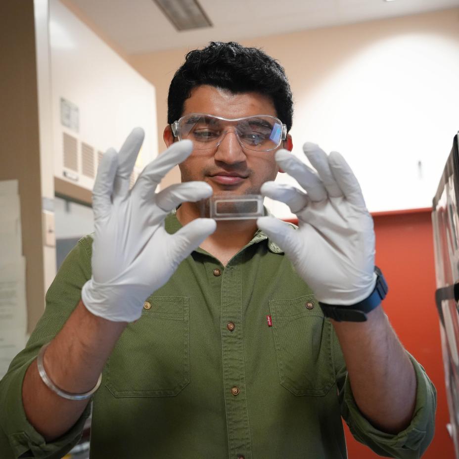 Pranav Dawar holds a NanoPOTs platform. He is wearing protective glasses and gloves.