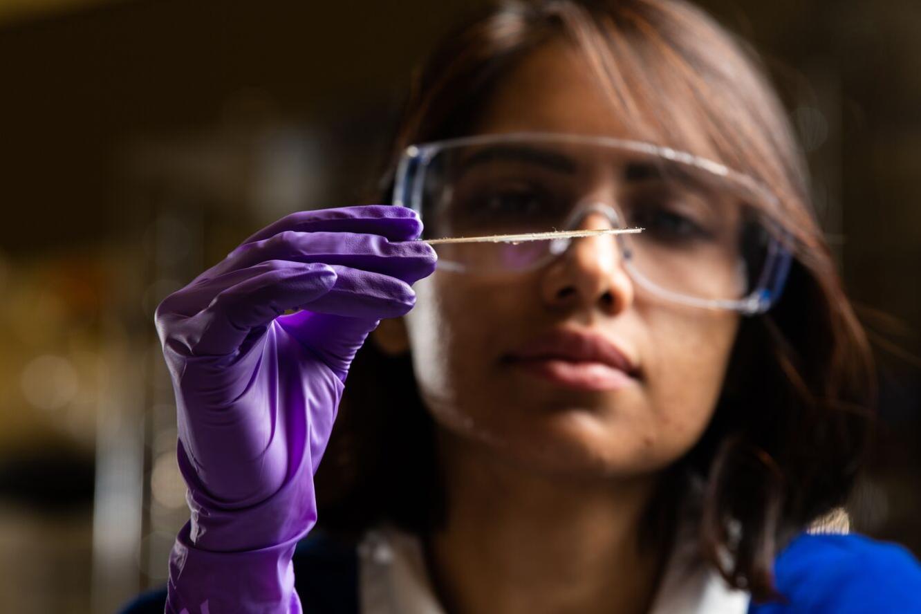 Researcher wearing glasses and purple glove holds thin device