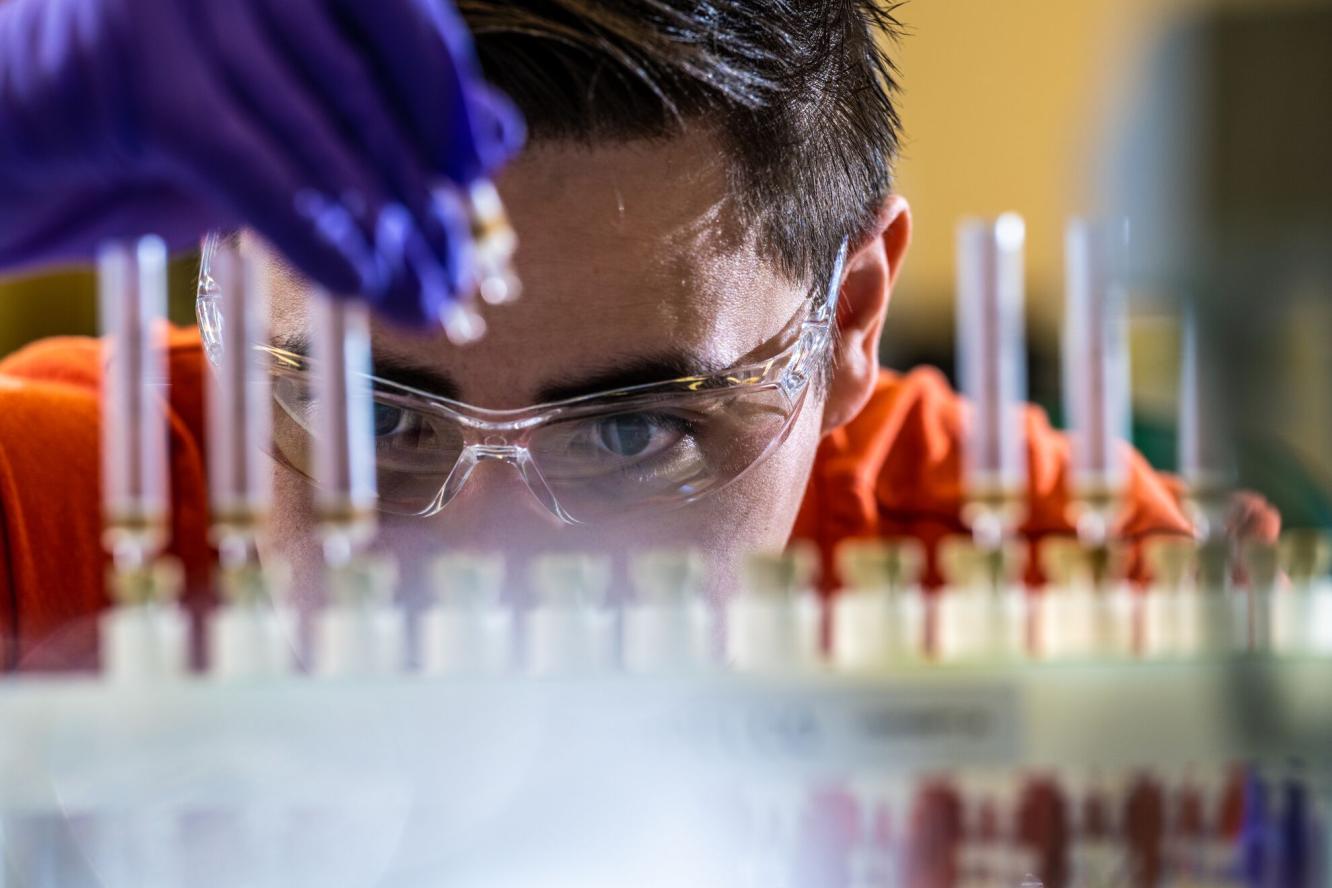 Researcher wearing gloves and safety glasses prepares samples in tubes