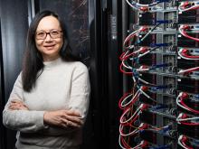 Photo of researcher Margaret Cheung smiling at the camera, standing next to a wall of computing equipment.