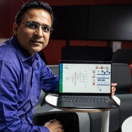 Portrait photo of Sumit Purohit holding a laptop in an office setting