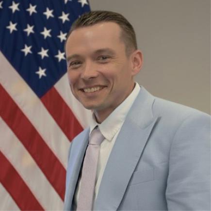 Photo of researcher Timothy Boe standing in front of an American flag.